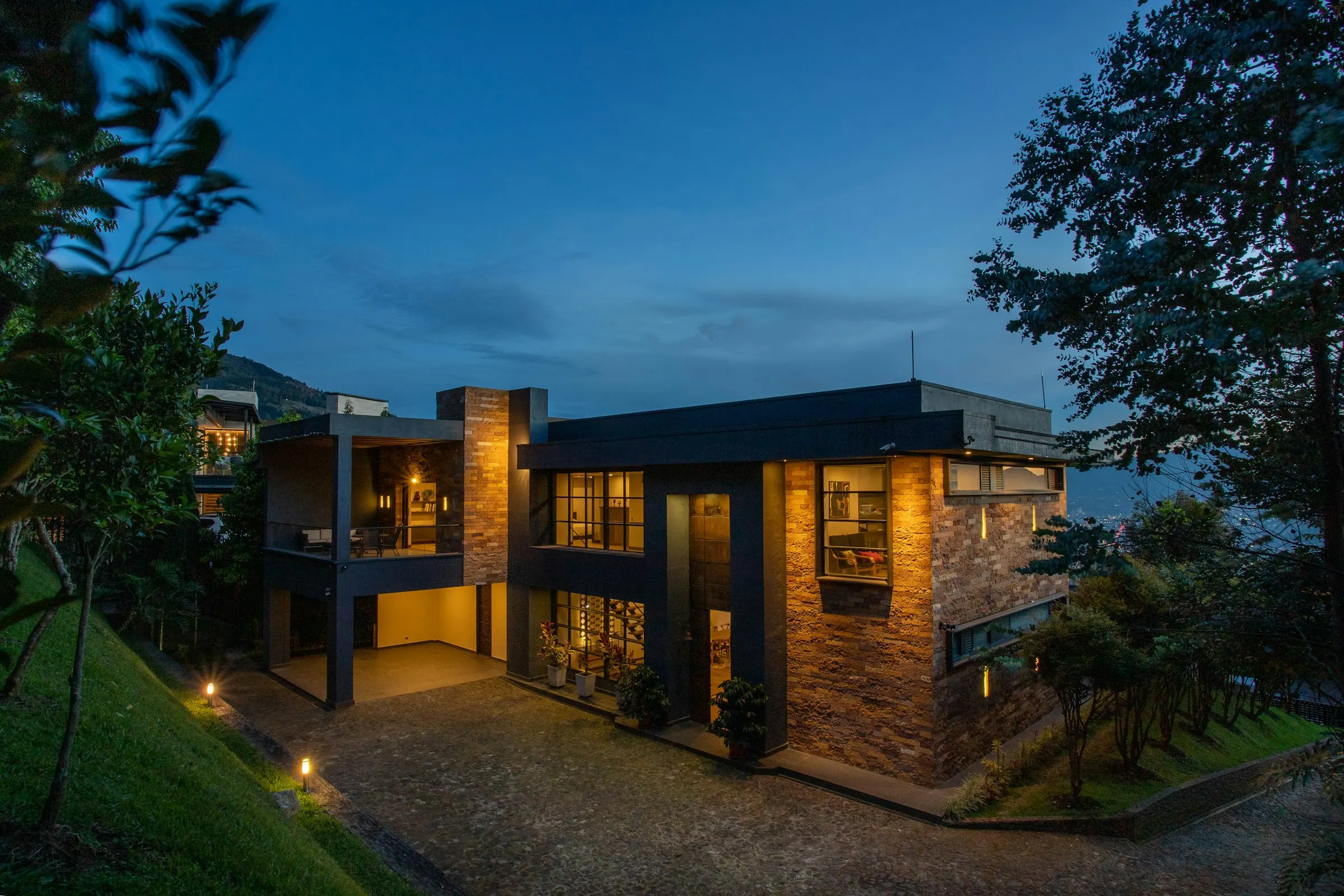 Moderne Villa mit Steinfassade am Hang, abends beleuchtet